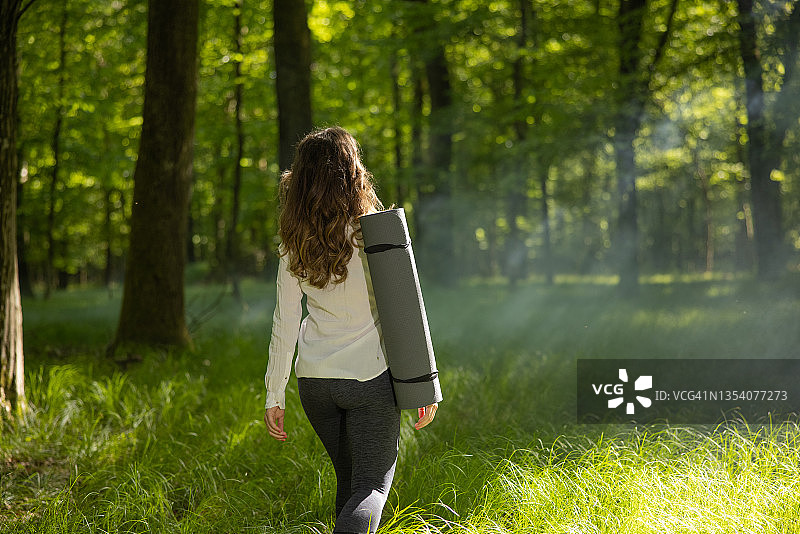 在森林里行走时，一个女人拿着瑜伽垫图片素材