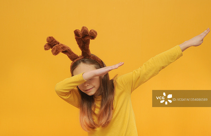 笑容动人的女孩与鹿耳朵在黄色t恤摆出彩色背景与复制空间。圣诞节的概念。图片素材