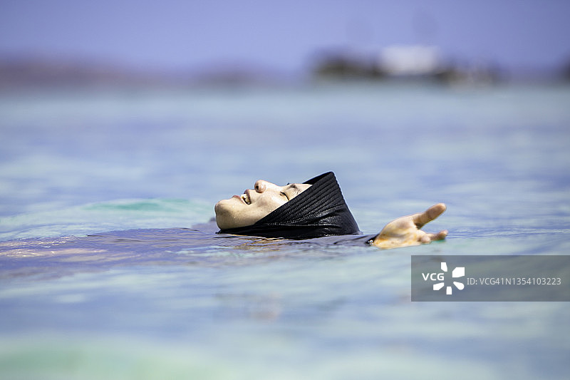 亚洲穆斯林妇女戴着头巾在海滩上游泳图片素材