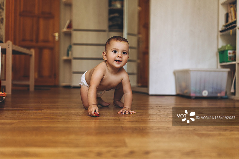 穿着尿布的小婴儿在家里的地板上爬图片素材