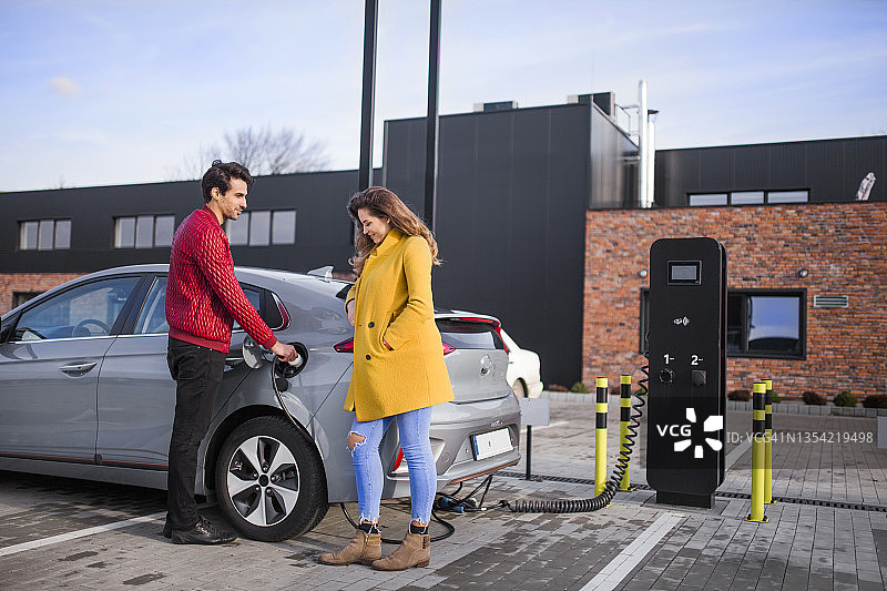 一对年轻夫妇在停车场给他们的电动汽车充电图片素材