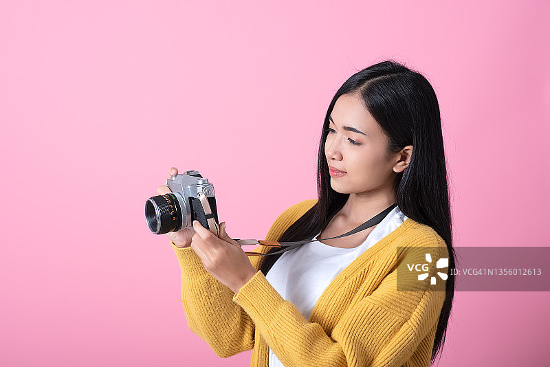 一个年轻的微笑的女人肖像拍摄与复古相机孤立在粉红色的背景图片素材