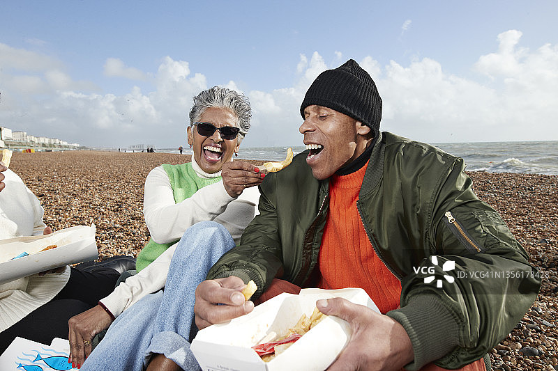 快乐的妇女在海滩上给男人喂鱼图片素材