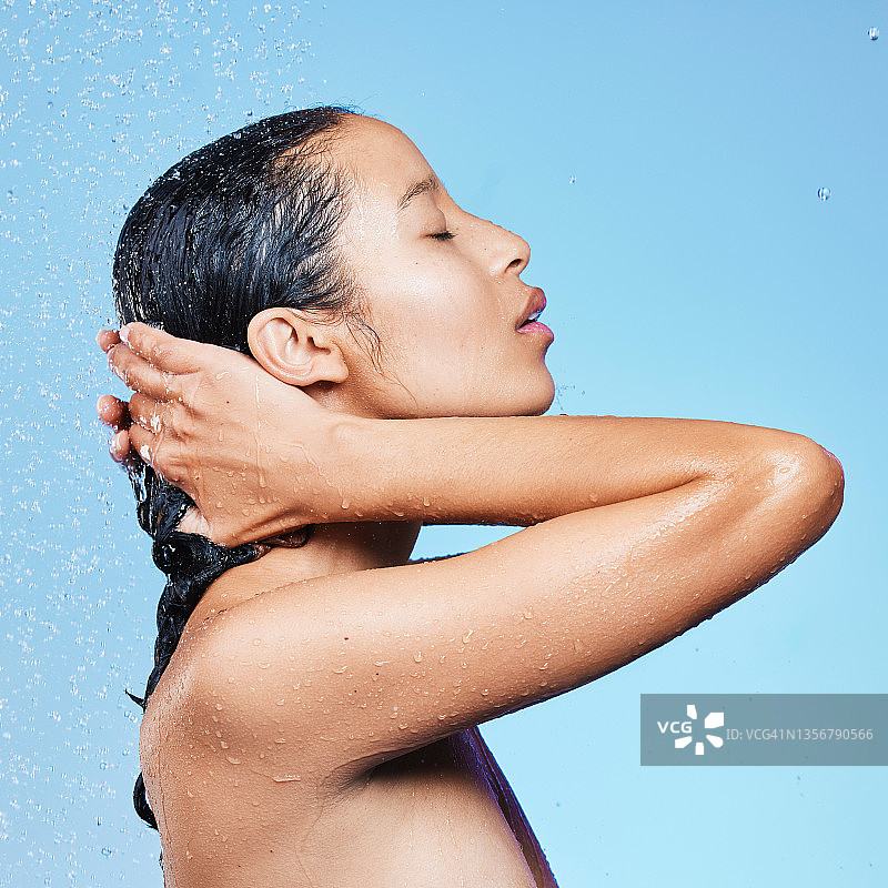 一个美丽的年轻女子在蓝色背景下享受清爽的淋浴图片素材