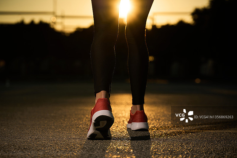 阳光下，女人穿着运动鞋在柏油路上行走图片素材