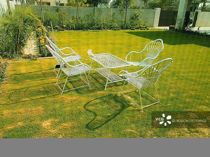 户外白色的铸铁椅子和桌子在郁郁葱葱的绿色草坪或花园的阳光下。图片素材