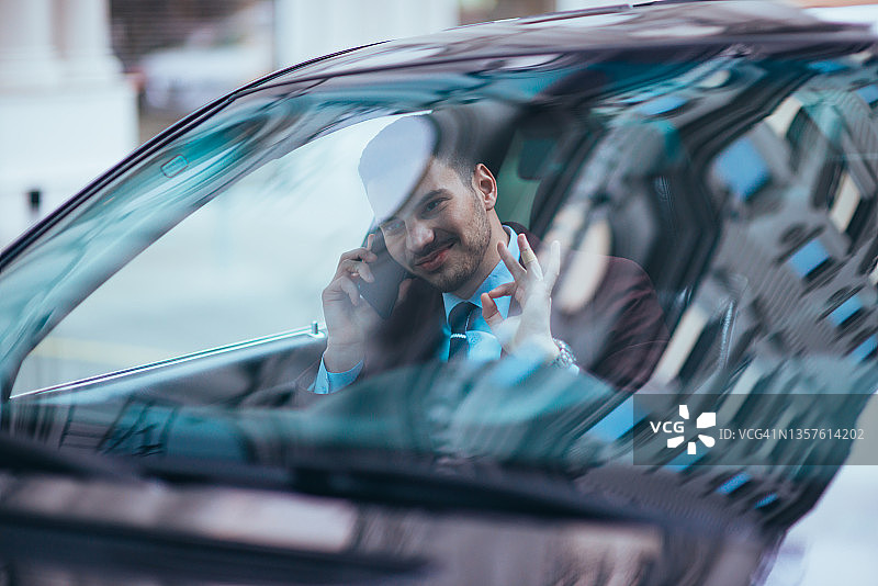 在繁忙的城市街道上，一位严肃的商人坐在他的豪华轿车的前座。图片素材
