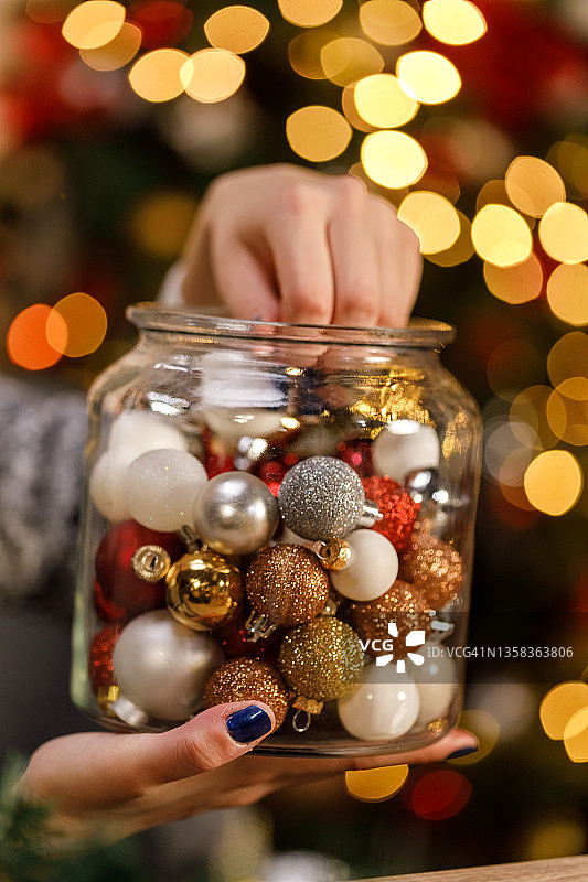 一个女人正在往玻璃罐里装满闪闪发光的圣诞装饰品图片素材