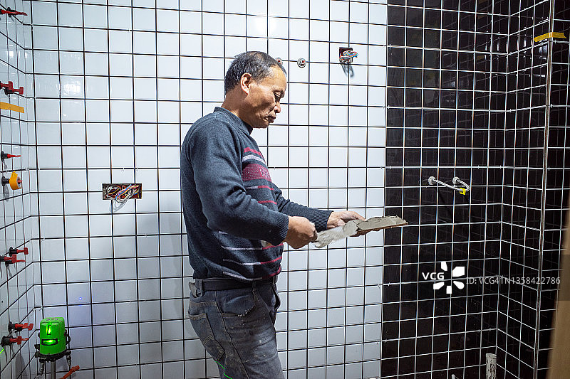 一位中年土方工人正在搅拌水泥和粘贴瓷砖。图片素材