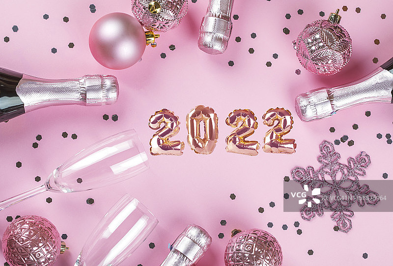新年快乐庆祝背景。粉色背景上的香槟瓶、眼镜和圣诞装饰品。图片素材