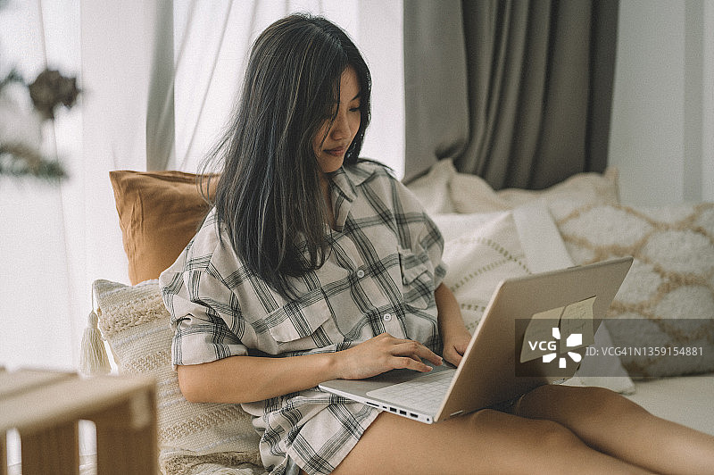 一个亚洲女学生坐在她的公寓地板上与笔记本电脑和笔记学习图片素材
