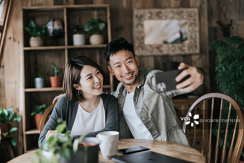 爱的年轻亚洲夫妇享受咖啡约会，在咖啡馆用智能手机自拍，快乐的微笑。一起分享快乐的时刻图片素材