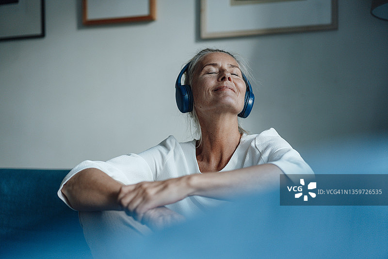 微笑的女人在家里戴着耳机听音乐图片素材