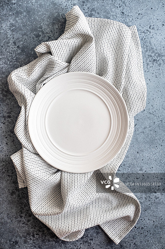 空的白色盘子上白色和黑色亚麻条纹餐巾折叠在灰色混凝土背景，俯视图。本空间图片素材