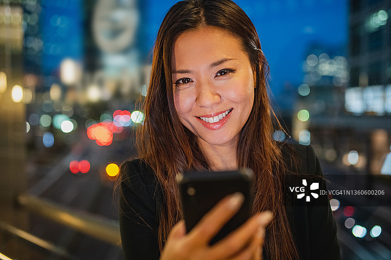 微笑的30多岁亚洲女商人在黄昏时使用智能手机图片素材