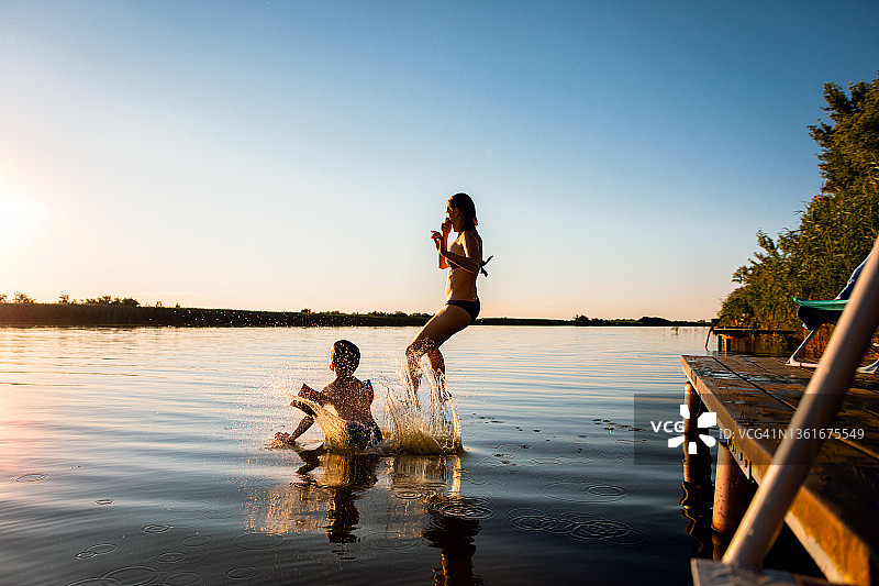 夏天的一天，母亲带着儿子享受假期，从码头跳进湖里。图片素材