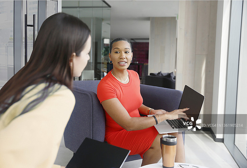 一名千禧一代的女性穿着时髦的休闲服装，在共同工作的空间里用笔记本电脑聊天。图片素材