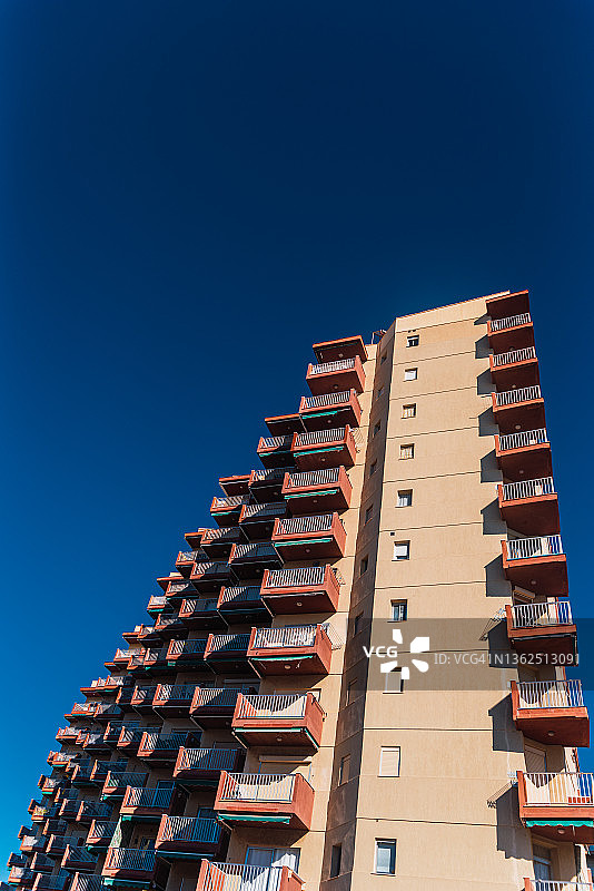蓝色的天空上有方形阳台的公寓楼。图片素材