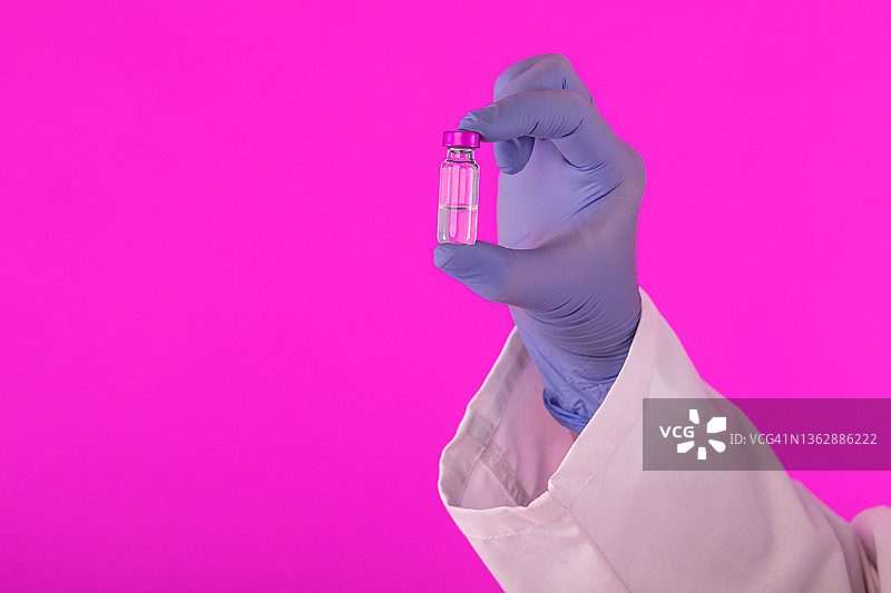 医生的手戴着乳胶手套，手里拿着一个疫苗瓶，用于抗击covid-19变种delta和omicron，背景为紫色。冠状病毒、大流行和健康概念。图片素材