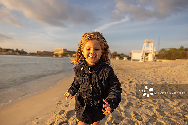 可爱的微笑的小女孩在日落的海滩上奔跑图片素材