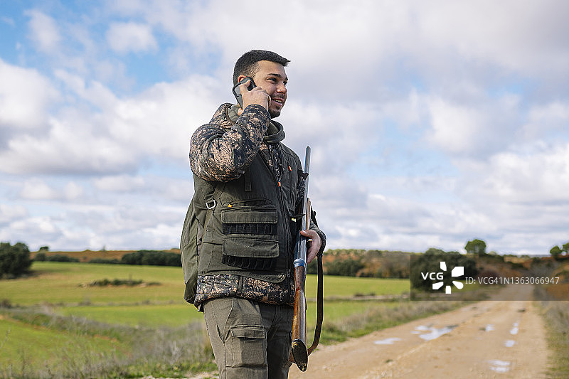 男性猎人的肖像，拿着枪和使用智能手机。图片素材