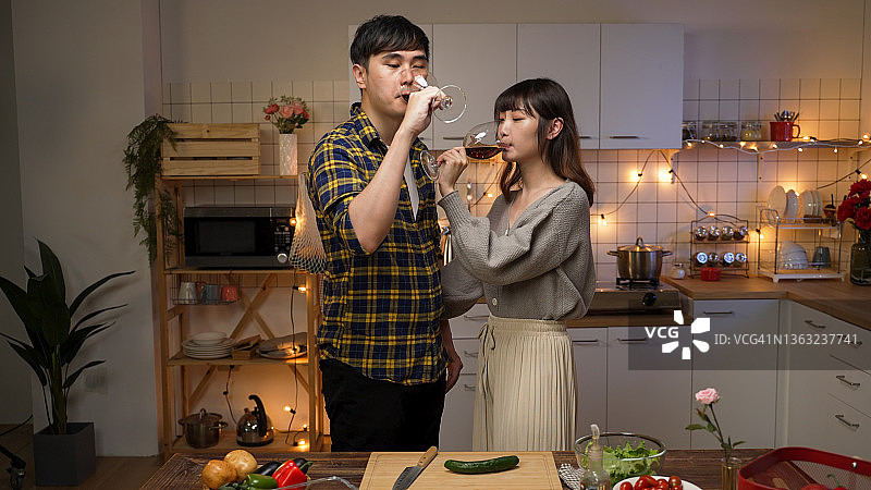亚洲情侣站在一起用红酒烤吐司庆祝情人节，晚上在家里厨房约会图片素材