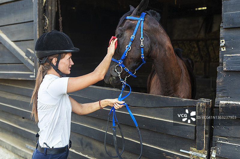 一个戴着马术头盔的年轻女子在照顾她的马。图片素材