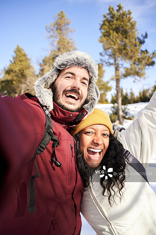 一对跨种族的年轻夫妇在雪景中自拍。图片素材