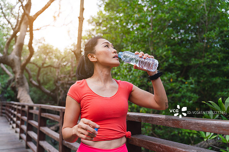 亚洲妇女在公园慢跑后喝一瓶水图片素材