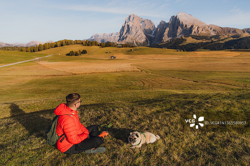 男性旅行者和他的狗在阿尔卑斯山的白云石山脉凝视日落的后视图图片素材