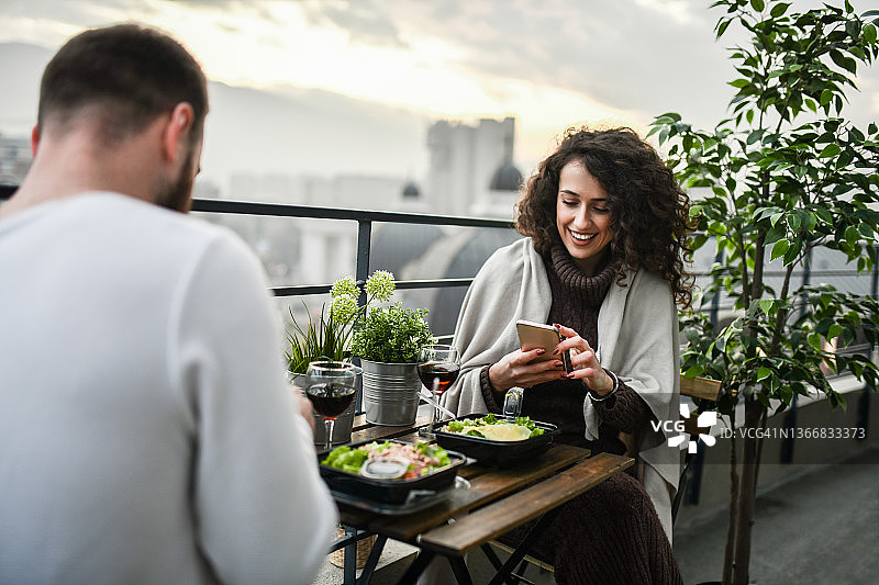 微笑的女性为社交媒体拍摄与男友在屋顶上的沙拉午餐图片素材