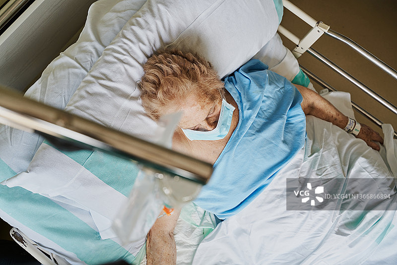戴着口罩的白人老年女性躺在医院的病床上与癌症作斗争。医学与健康理念图片素材