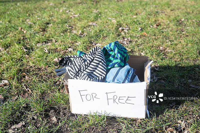 一箱衣服放在公园的草地上捐赠。图片素材
