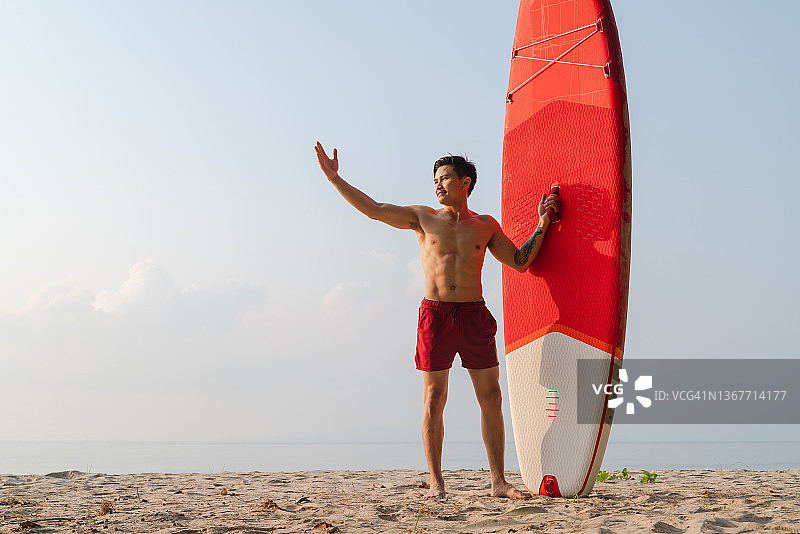 亚洲年轻运动员的肖像站在沙滩上站起来的冲浪板图片素材