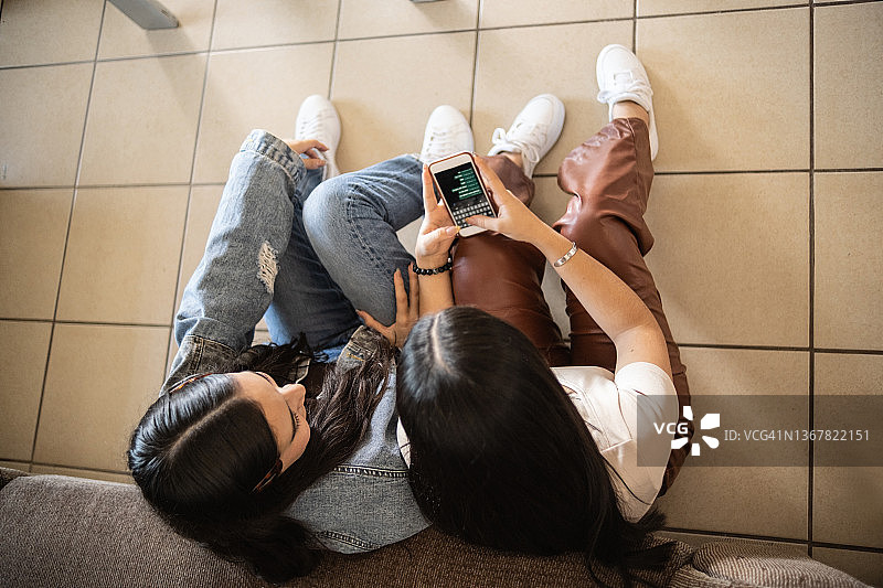 姐妹们坐在家里的地板上用智能手机图片素材