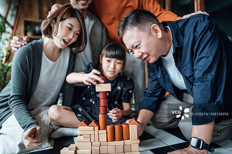 裁剪拍摄的快乐的多代亚裔家庭，祖父母，父母和孩子坐在客厅的地板上一起玩木制积木在家里图片素材