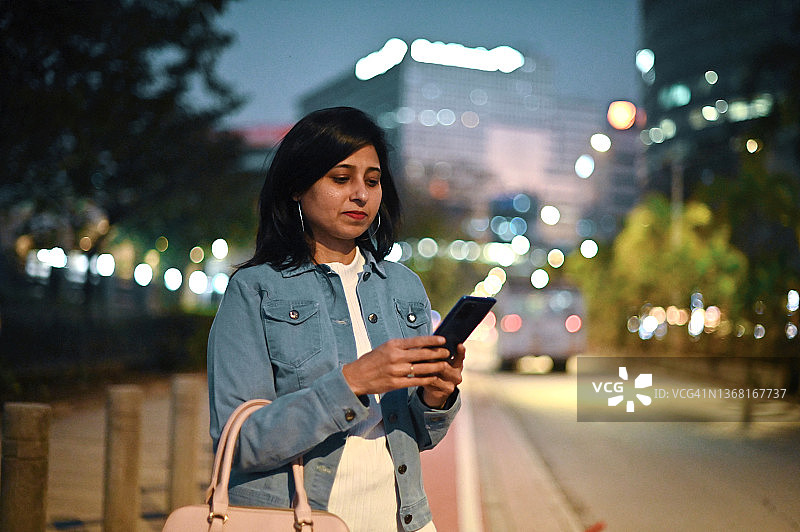 一位妇女站在城市街道上，在商业区使用手机图片素材