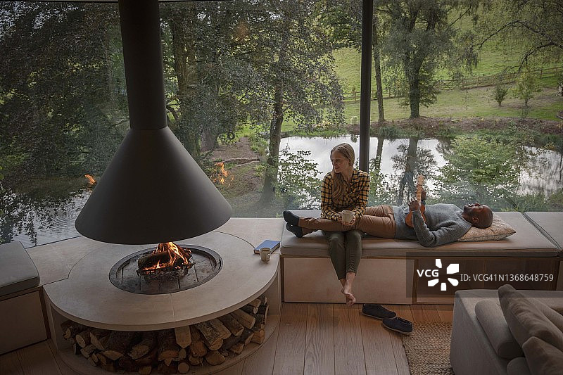 英国，德文郡，蒂弗顿，一对夫妇在现代住宅的壁炉旁放松图片素材
