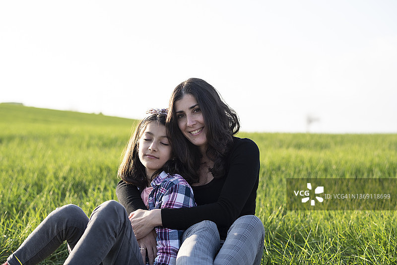母亲和女儿享受春天的拥抱微笑和快乐的谷物草地图片素材