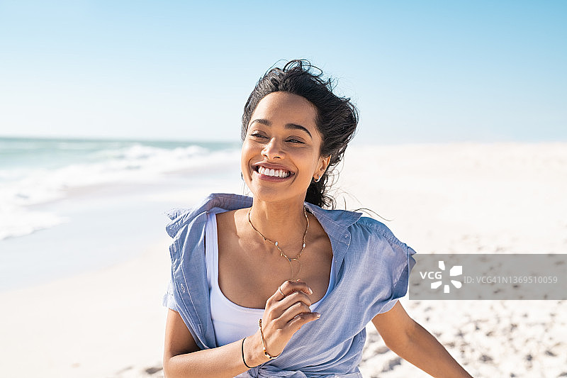 快乐微笑的女人在沙滩上跑步在一个美丽的夏日图片素材