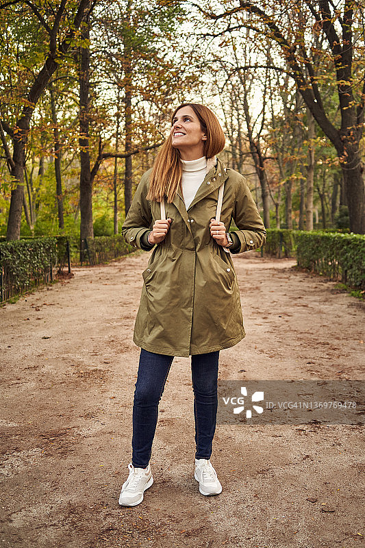 穿着外套微笑的女人站在秋天的公园里图片素材