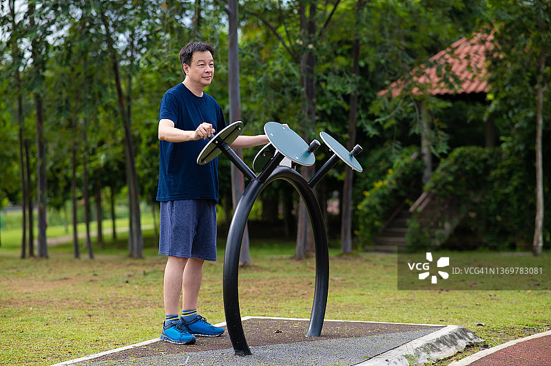 图为，一名亚洲中年男子在小区花园的椭圆机上锻炼图片素材