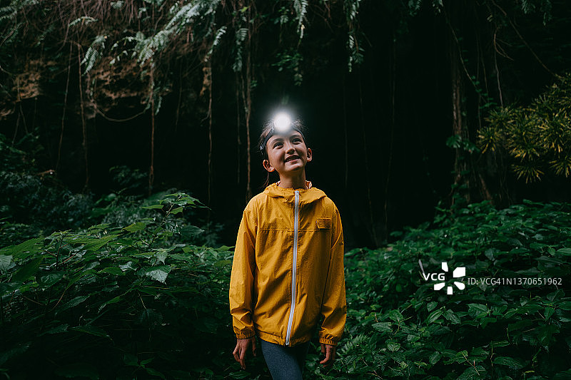 在日本冲绳，一名带着头灯的小女孩徒步穿越雨中的丛林洞穴图片素材