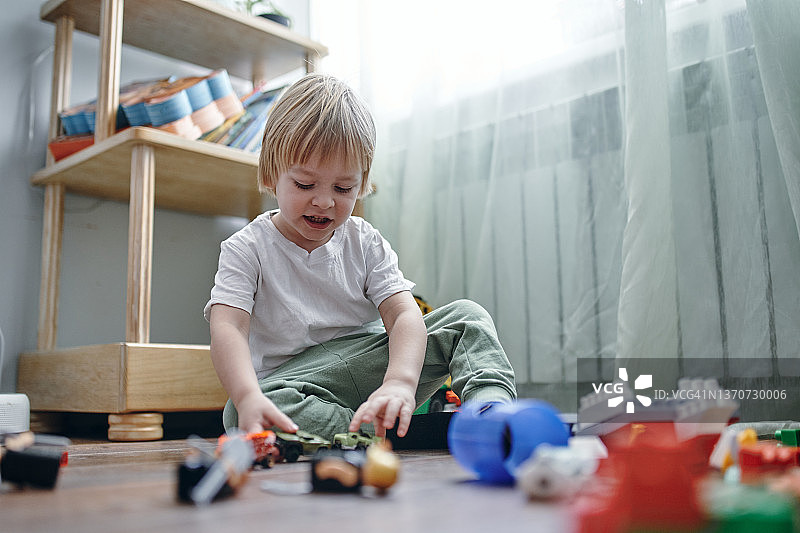 一名3岁的金发男孩穿着白色t恤，坐在木地板上玩着五颜六色的方块图片素材