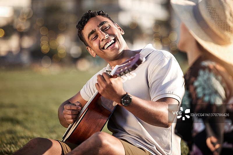 这张照片拍摄的是一个年轻人在和女朋友野餐时弹吉他图片素材