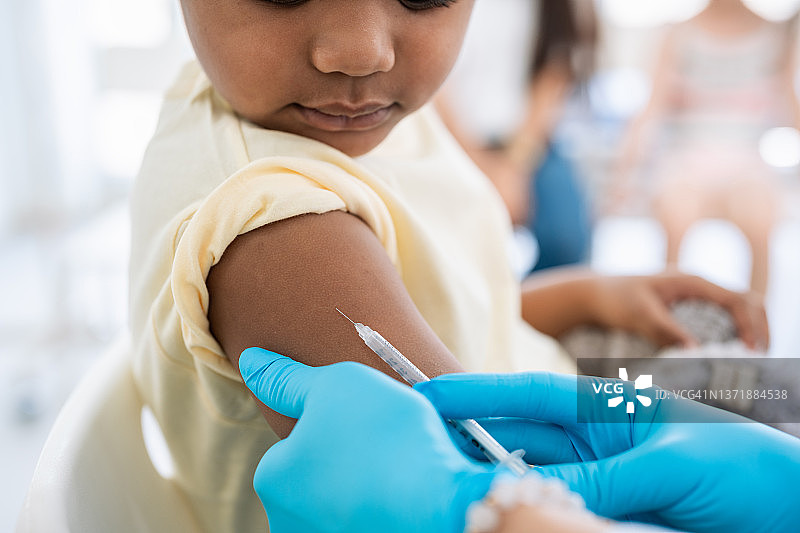 免疫接种。保护儿童远离疾病。戴着医用手套的护士在给小病人注射。勇敢的男孩在医生的办公室打流感疫苗，看针图片素材