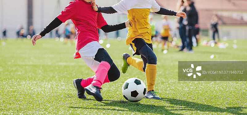 男生和女生在踢足球。孩子们玩得开心，踢足球。穿着粉红色足球服的女孩正在踢球图片素材