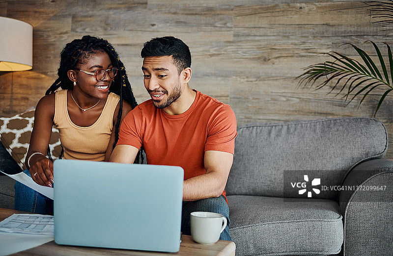 这张照片拍摄的是一对年轻夫妇坐在家里的客厅里，用笔记本电脑计算他们的财务状况图片素材