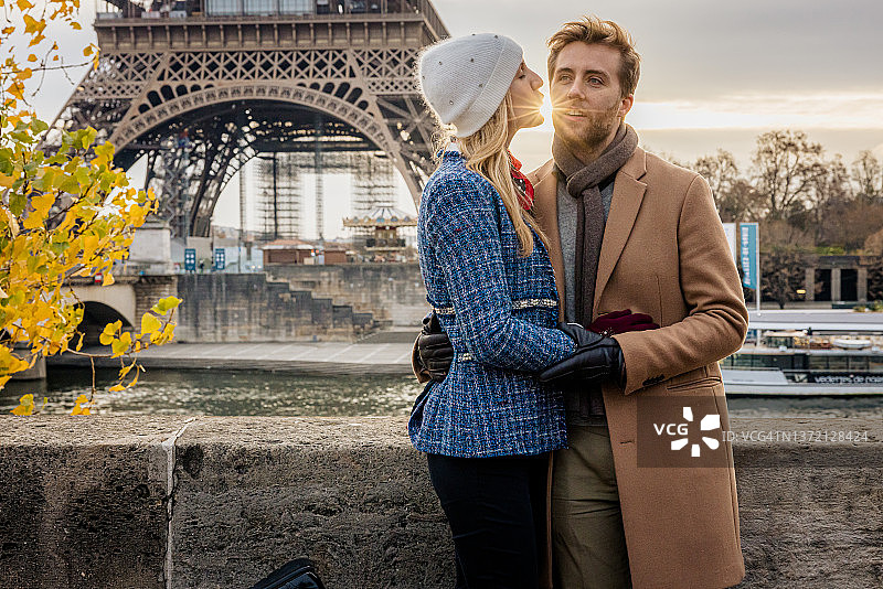 女友在巴黎埃菲尔铁塔前亲吻男友，傍晚，阳光在她的双唇和男友的脸颊之间图片素材