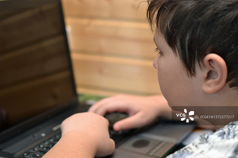 一个十几岁的男孩在用笔记本电脑。图片素材